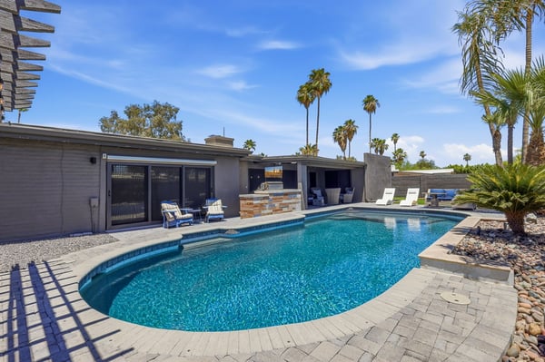 Sweeping backyard view showcases the sparkling pool, covered entertaining patio, built-in BBQ, paver decking, and thoughtfully designed outdoor gathering spaces in Scottsdale.