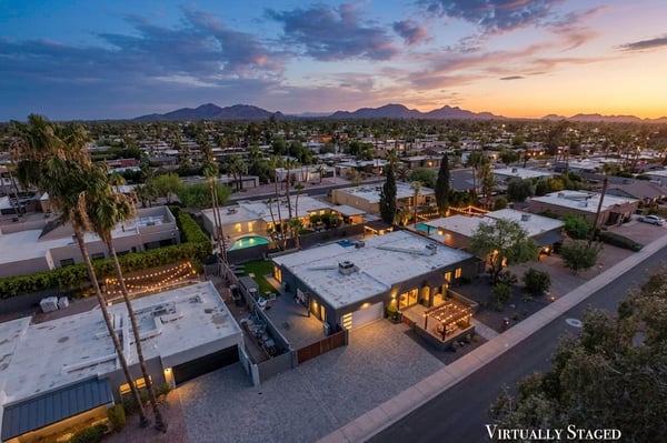 Twilight aerial showcases the Scottsdale neighborhood, surrounding mountain views, and the property's beautifully illuminated exterior, emphasizing its exceptional setting.