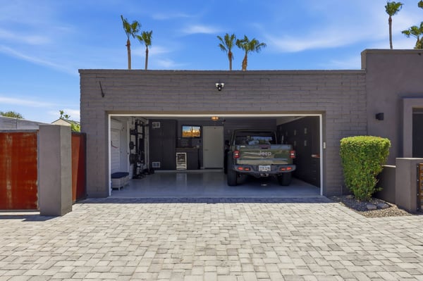 Exterior garage view showcases the oversized paver driveway, contemporary garage door, and organized interior with built-in cabinetry. A polished Scottsdale property with exceptional functionality.