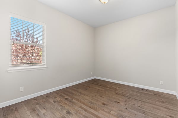 Spacious, sunlit room with a large window and hardwood flooring, perfect for various design possibilities.