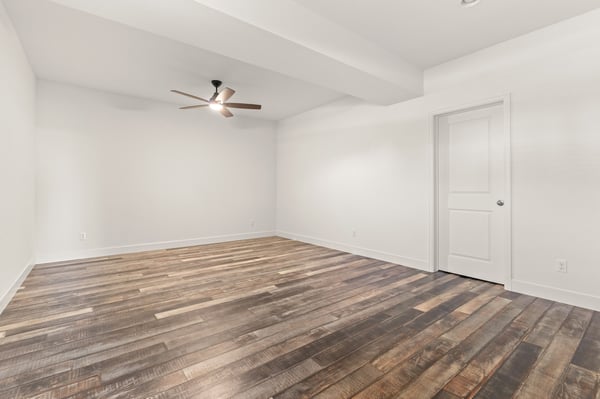 Spacious room featuring warm wood flooring, a ceiling fan, and natural light options for customization.