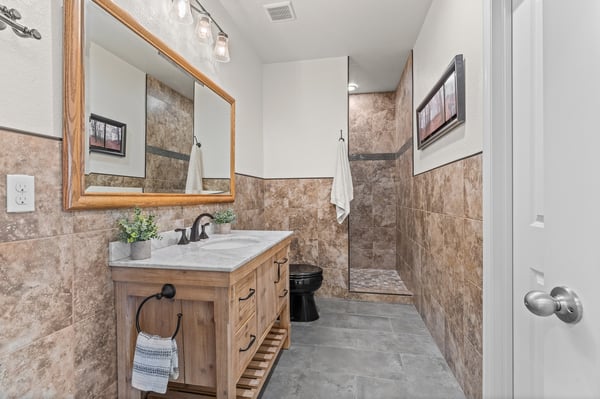 Contemporary bathroom featuring natural stone accents, a spacious shower, and a sleek wooden vanity.