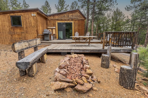 Cozy cabin nestled among trees, featuring a spacious deck and fire pit for outdoor gatherings.