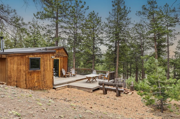Cozy cabin nestled among towering pines, featuring an inviting deck for outdoor relaxation and enjoyment.