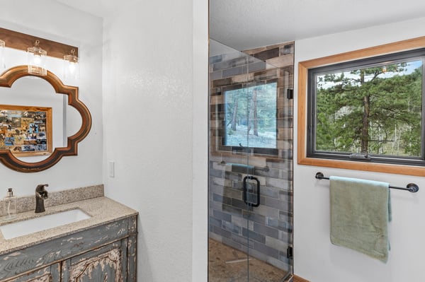 Bright bathroom featuring a modern glass shower and a beautifully framed mirror, with nature views beyond.