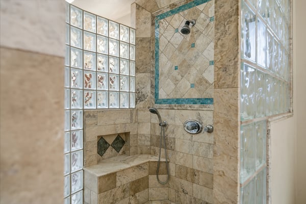 Experience a uniquely designed shower space featuring intricate tile work and natural light from glass blocks.