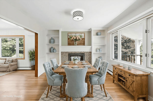 Bright dining area featuring built-in shelves, a cozy fireplace, and large windows overlooking a lush landscape.