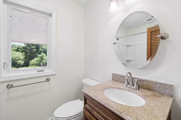 Bright bathroom featuring a circular mirror, granite countertop, and convenient window for natural light.