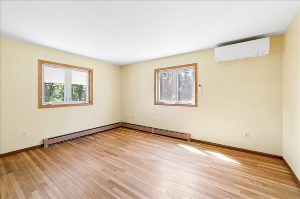 Bright and open room featuring hardwood floors and natural light from two large windows.