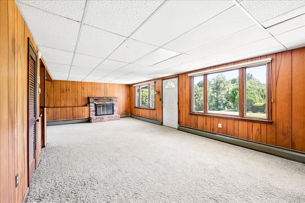 Spacious living area with abundant natural light, featuring wood paneling and cozy fireplace, ready for personalization.