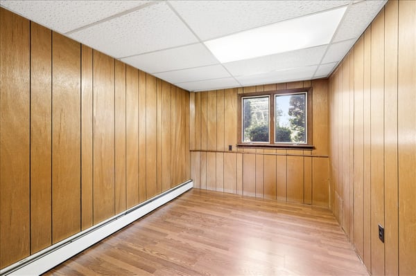 Spacious room with warm wooden paneling, offering natural light and potential for customization.
