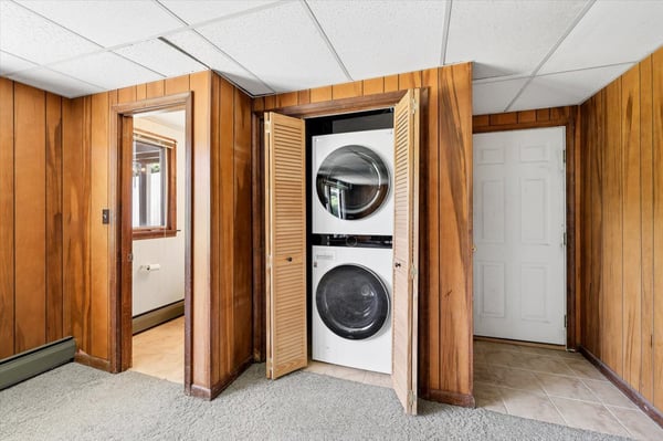 Convenient laundry area with stacked washer and dryer, featuring warm wood paneling and easy access.