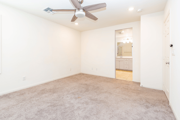 Spacious, versatile room with soft carpeting and a ceiling fan, leading to a modern bathroom.