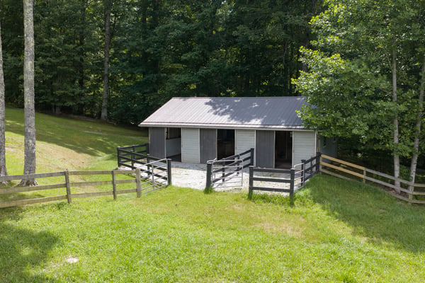 This property features a spacious barn surrounded by lush greenery and rustic fencing, ideal for outdoor enthusiasts.