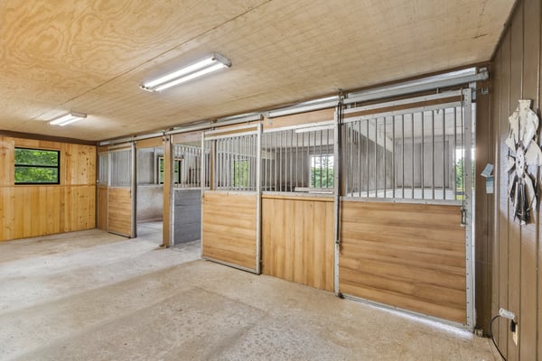 This spacious equestrian facility features multiple stalls, ample lighting, and easy access to outdoor areas.