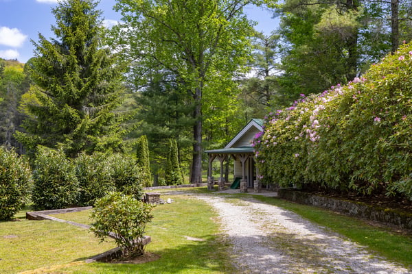 This picturesque property features lush landscaping, a winding gravel drive, and a cozy entrance nestled among the trees.