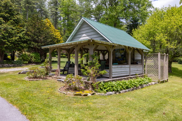 Cozy cottage with a green metal roof, surrounded by lush gardens and inviting outdoor seating.