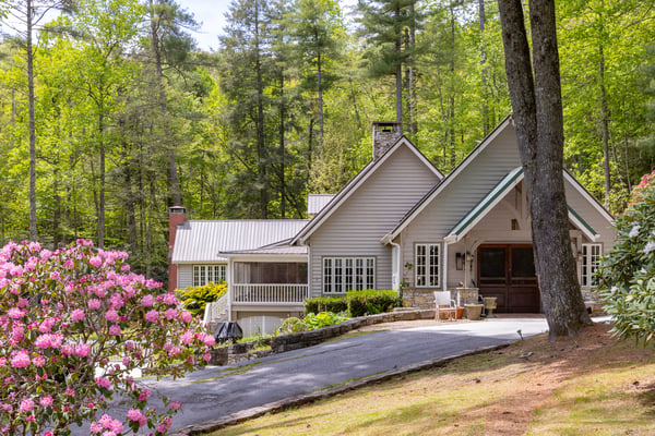 Nestled among lush greenery, this inviting home features a spacious driveway and warm outdoor gathering areas.