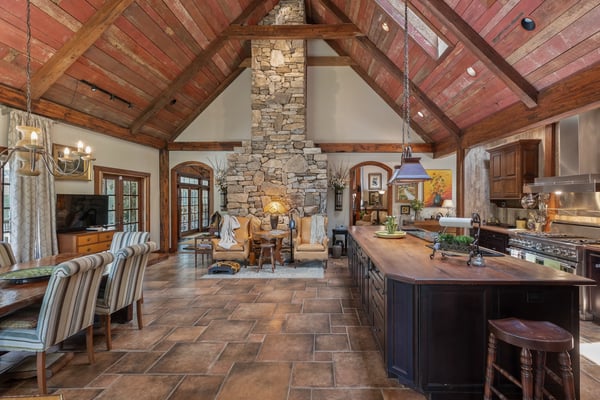 Spacious open-concept kitchen and dining area featuring a striking stone fireplace and rustic wooden beams.
