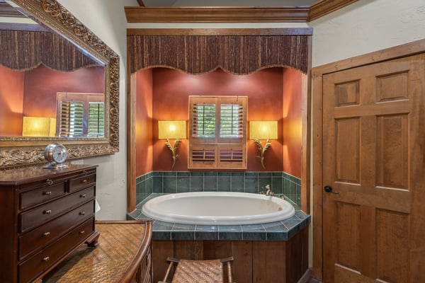Relax in this inviting bathroom featuring a corner tub, warm lighting, and rich wooden accents.