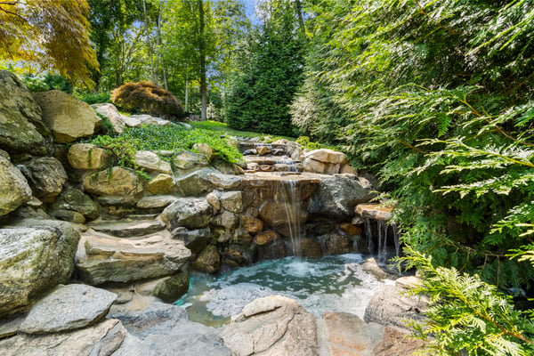Discover a tranquil oasis featuring a natural stone waterfall and lush greenery, perfect for relaxation.