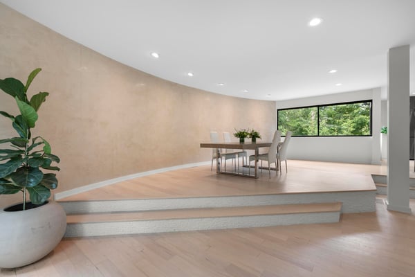 Spacious dining area featuring a unique curved wall and large windows, offering abundant natural light and greenery views.