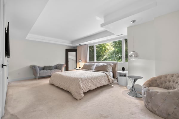 Spacious bedroom featuring large windows with natural light, plush carpet, and modern furnishings for comfort.
