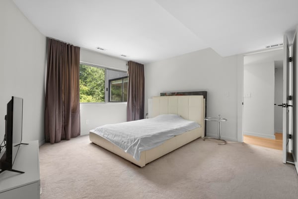 Bright, spacious bedroom featuring large windows, neutral tones, and access to nearby bathrooms for convenience.