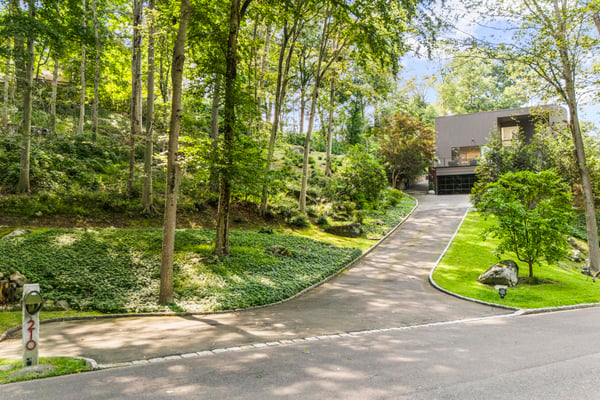 This unique property features a generous driveway leading to a contemporary home nestled amongst lush trees.