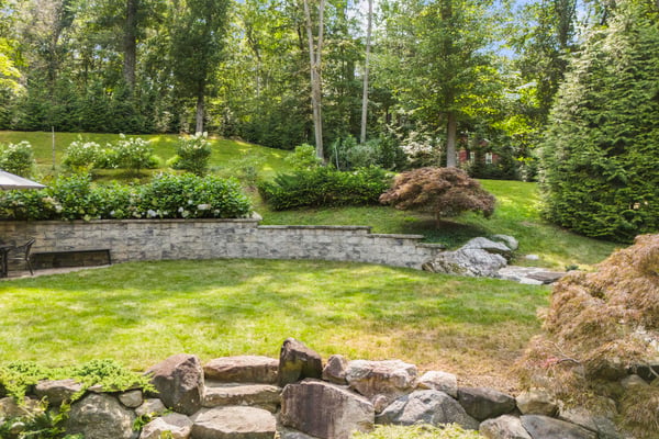 Lush, landscaped backyard features tiered greenery, stone walls, and a tranquil space for outdoor gatherings.