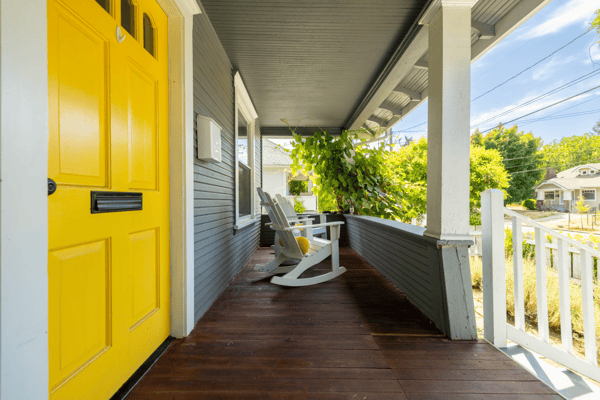 Welcoming porch featuring a vibrant yellow door and peaceful seating, perfect for enjoying neighborhood views.