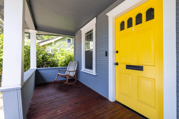 Bright yellow door welcomes you to this inviting porch, perfect for relaxing and enjoying the outdoors.