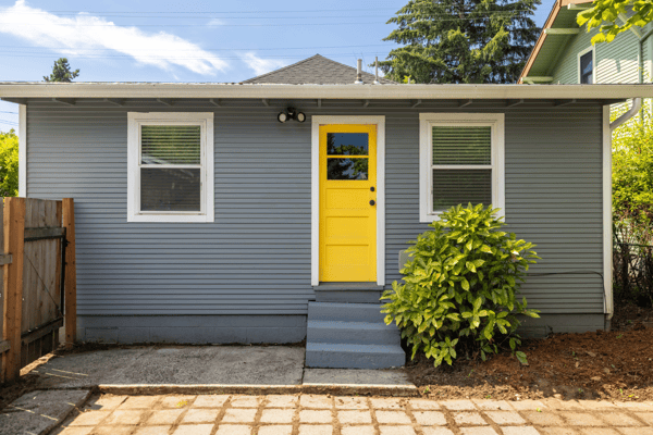 Bright and inviting home featuring a distinctive yellow door, ample natural light, and a spacious front yard.