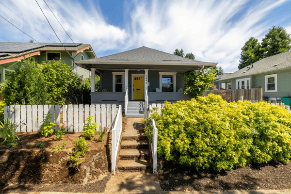 This inviting home features a vibrant yellow door, lush landscaping, and a welcoming front porch.