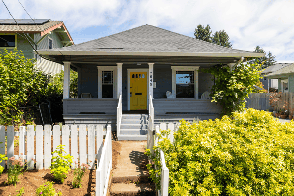 This inviting home features a bright yellow door, spacious porch, and vibrant landscaping in a friendly neighborhood.