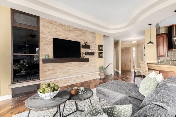 Sophisticated living area featuring a stacked stone accent wall, media center, rich wood flooring, and open-concept design. The seamless connection to the kitchen creates an inviting space for gathering and entertaining.