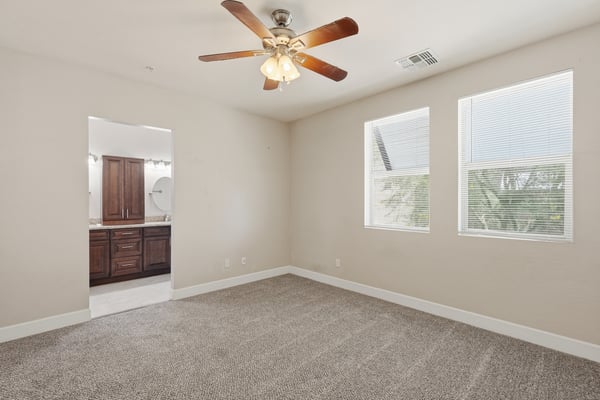 Spacious primary suite with plush carpeting, large windows, and a ceiling fan for added comfort. Designed to provide a peaceful retreat at the end of the day.