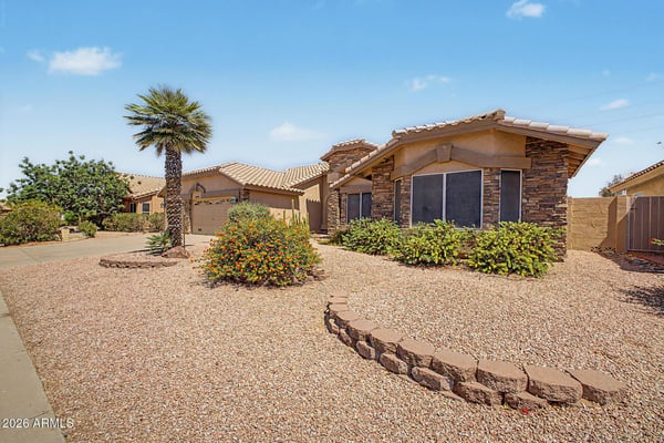 Professionally maintained desert landscaping surrounds the home with colorful blooms, mature palm trees, and decorative rock features. The inviting front yard reflects the low-maintenance lifestyle many buyers seek.