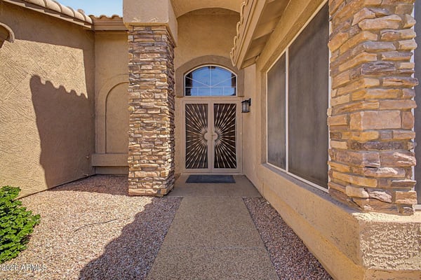 Elegant stone columns and a covered entry create a striking first impression. The decorative security door and architectural accents add both style and functionality to the home's welcoming entrance.