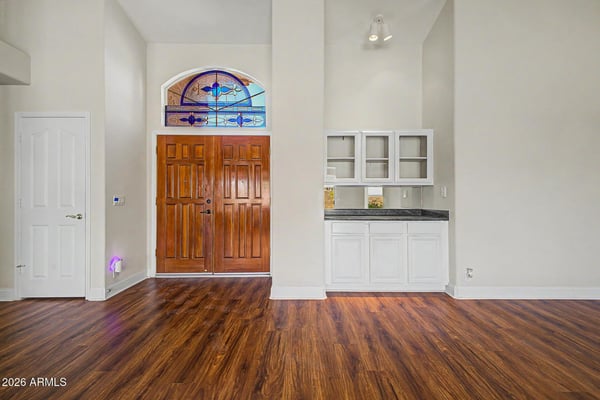 Tall ceilings, warm wood-look flooring, and decorative stained glass details create a memorable entry experience. Built-in storage cabinetry adds convenience while maintaining the home's clean, open aesthetic.