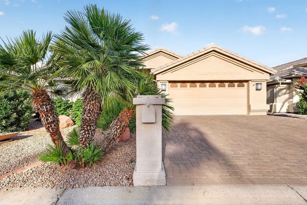 Tropical-inspired palm trees and manicured desert landscaping create a striking first impression. The home's clean exterior lines and paver driveway contribute to its move-in ready presentation.