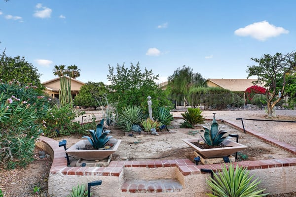 Decorative planters, mature desert vegetation, and charming pathways create a tranquil backyard setting. This thoughtfully landscaped outdoor space offers beauty with minimal maintenance.