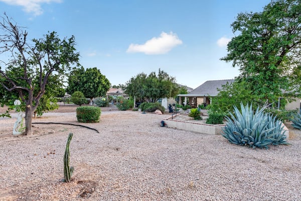 Established desert landscaping, mature shade trees, and decorative garden features create an inviting outdoor environment. The spacious design enhances privacy and curb appeal.