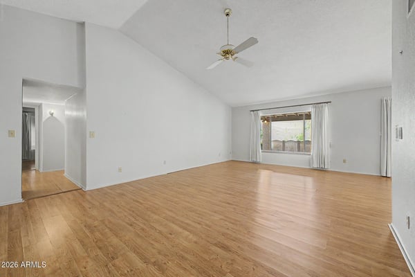 Vaulted ceilings and expansive living space define this bright great room. Wood-look flooring and natural light create an inviting setting perfect for entertaining guests or enjoying quiet evenings at home.