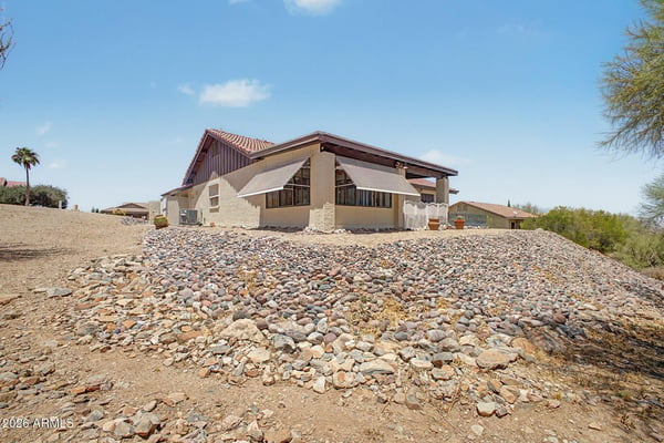 This rear exterior view highlights the home's attractive architecture, mature desert landscaping, and elevated setting. The spacious lot and low-maintenance grounds contribute to the property's appeal in Fountain Hills.