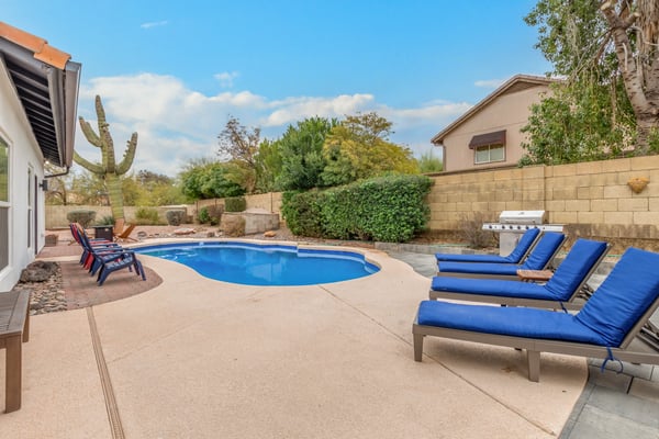 Well-appointed outdoor space featuring a sparkling pool, sun loungers, grilling area, and mature landscaping. Ideal for enjoying Scottsdale's outdoor lifestyle and entertaining guests.