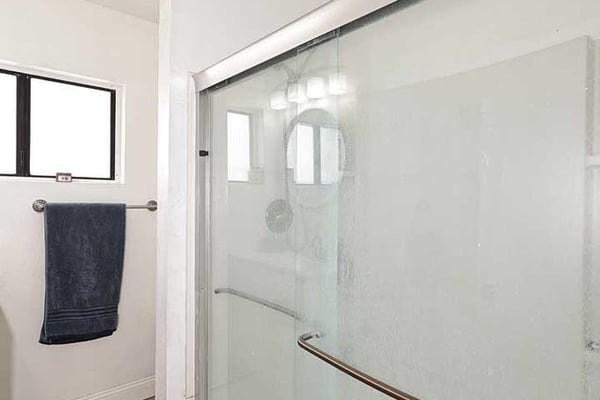 A large glass shower enclosure highlights this refreshed bathroom space. Bright finishes, natural light, and modern updates contribute to the clean and functional design.