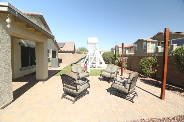 The large paver patio creates the perfect outdoor entertaining space, complemented by artificial turf, mature shrubs, and plenty of seating for relaxing or hosting guests.