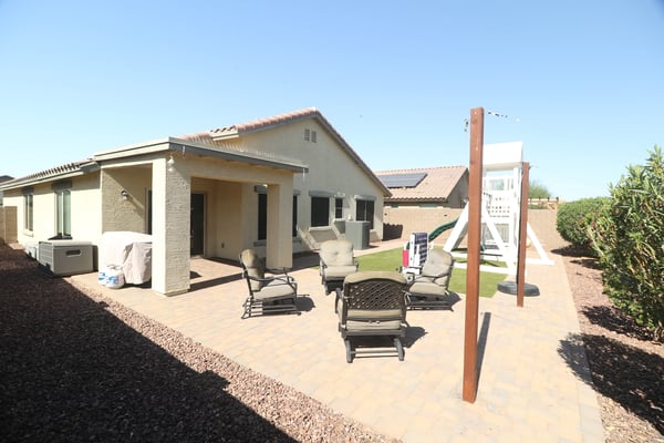 A covered patio overlooks the spacious backyard featuring paver hardscaping, low-maintenance landscaping, and artificial turf. Designed for comfortable outdoor enjoyment throughout the year.