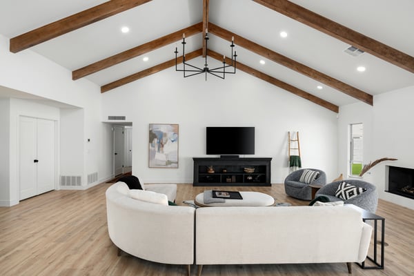 Vaulted ceilings, exposed beams, expansive windows, and beautiful flooring define this sophisticated living room, offering a bright and welcoming space ideal for relaxing or entertaining.